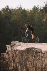 side view of trial biker balancing on rocky cliff outdoors