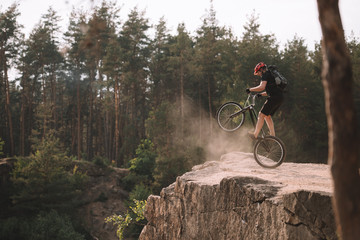 Fototapeta premium trial biker balancing on back wheel on rocks outdoors