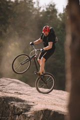 handsome trial biker balancing on back wheel on rocks outdoors