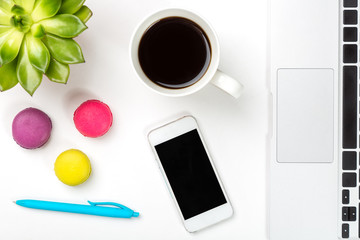 Conceptual workspace or business concept. Green plant in a pot, cup of coffee, colorful macaroons, blue pen, laptop and modern mobile cell phone on white background
