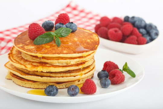 Homemade american pancakes, with fresh blueberries, raspberries and maple syrup on a white background