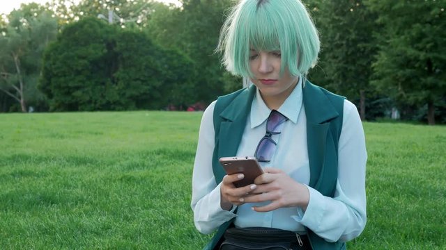 Pretty student girl reads messages and watches photos on mobile phone and has a rest in city park