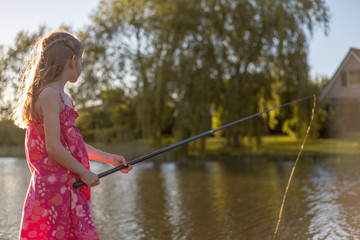 Ein Mädchen steht mit Angelrute an einem See