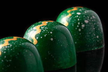 Luxury handmade chocolate candies on black background. Green candies with multicolored drops. Product concept for chocolatier. Close-up