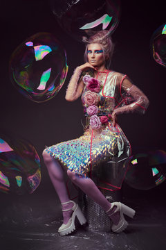 Gorgeous woman in biofuture pompadour style. Female in fashion transparent raincoat with splendid make up and hairstyle, photoshoot through soap bubble