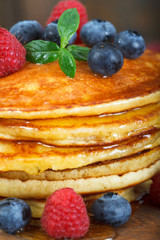 Stack of freshly baked american pancakes with maple syrup, blueberries and raspberries on top. Closeup image..