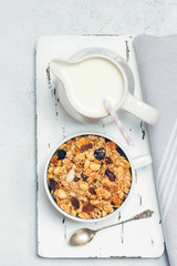 Cup of muesli with tropical fruits and white milk jug on wooden board. Concept of healthy eating in pure tones.
