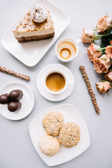Obraz na płótnie Canvas Delicious fresh morning espresso coffee, three cookies, a piece of cake, chocolate sticks, three chocolates and a bouquet of roses on the pastel grey background, top view, flat lay