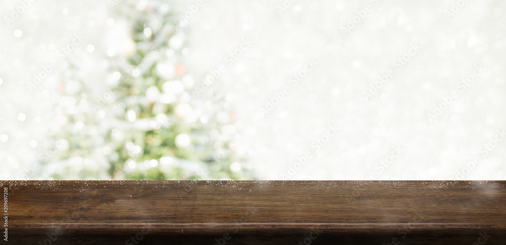 Poster Empty dark brown wooden table top with abstract muted blur christmas tree and snow fall background with bokeh light,Holiday backdrop,Mock up banner for display or montage of product.