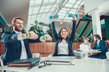 Two workers exercising with dumbbells at desk.