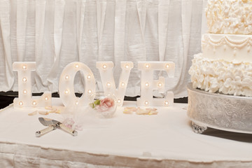 Love sign near white wedding cake 