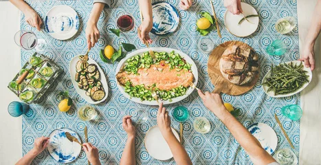 Tuinposter Family or friends summer party or seafood dinner. Flat-lay of group of mutinational people with different skin color at big table eating delicious food together. Summer gathering or celebration © sonyakamoz