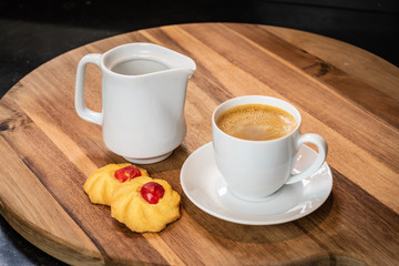 Coffee break concept: Creamy coffee, jug of milk and fresh baked cookies with candied cherry on a wooden board.