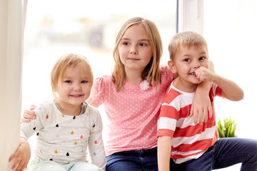 childhood, leisure and family concept - happy little kids hugging at window