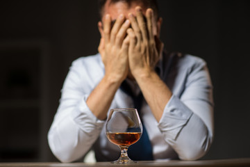 alcoholism, alcohol addiction and people concept - male alcoholic drinking brandy on table at night