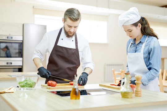 Portrait of professional chef working in restaurant kitchen with su-chef, both cutting vegetables standing at wooden workstation, copy space