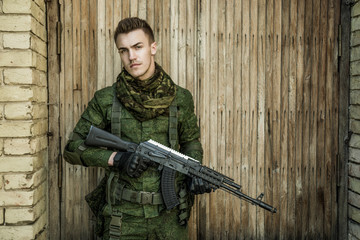Young male military soldier with a rifle posing against wooden background