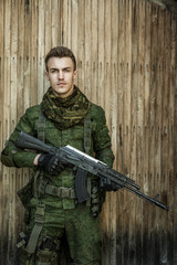 Young male military soldier with a rifle posing against wooden background