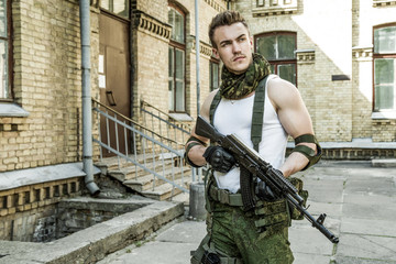 Young male military soldier with a rifle near the old building