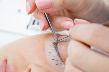 Beautiful Woman with long lashes in a beauty salon. Eyelash extension procedure. Master of tweezers is working