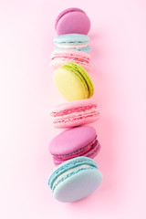 The vertical row of colorful macarons on pink background.