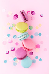 The row of colorful sweet macarons on pink background decorated with confetti. Top view, vertical.