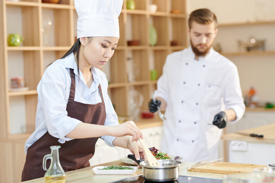 Portrait of female Asian chef cooking delicious dishes while working in modern restaurant kitchen, copy space