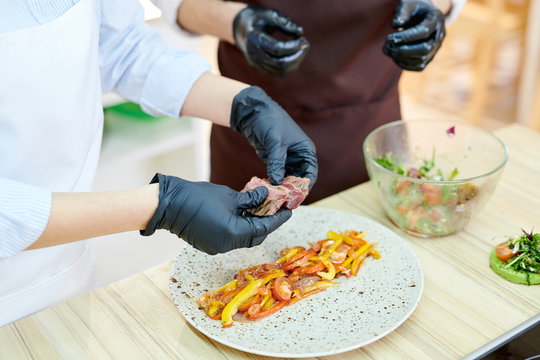 High angle close up of unrecognizable female chef serving dishes while cooking in modern restaurant kitchen