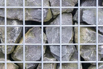 Wall of grey rocks behind a light grey metal grid background  