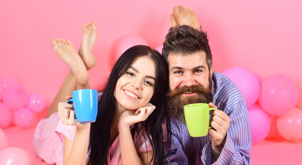 Obraz na płótnie Canvas Man and woman on smiling faces lay, pink background. Couple in love drink coffee in bed. Couple relax in morning with coffee. Family tradition concept. Man and woman in domestic clothes, pajamas.