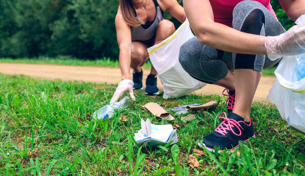 Women crouching with bag picking up trash doing plogging