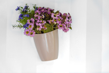 Colourful flowers in glass vase, spring decoration hanging on white metal wall, decoration concept. 