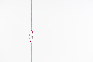 Fishing hook attached to a rope hanging on a red together on white background.