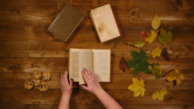 Autumn concept top view. Books, maple leaves, bake the old wooden table. Woman scrolls through book pages