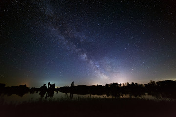 Space with stars in the night sky. The landscape with the river and trees is photographed on a long exposure.