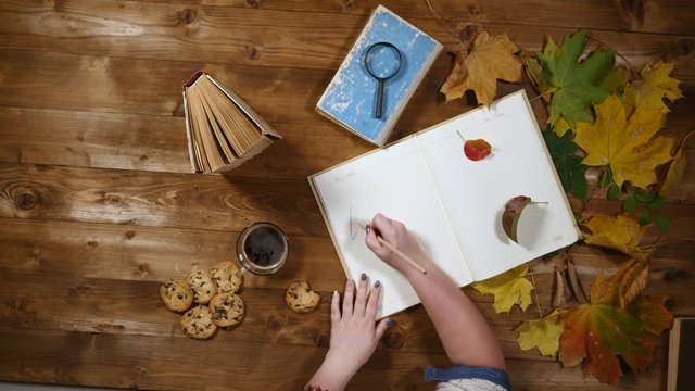 Autumn concept top view. Books, maple leaves, tea on the old wooden table. Woman writing notes in the notebook