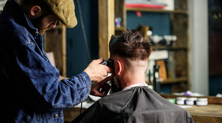 Barber with clipper trimming hair of client, rear view. Working process concept. Barber with hair clipper works on short haircut on teple, barbershop background. Hipster client getting short haircut