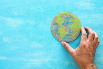 top view image of man hand holding earth globe over blue wooden background.