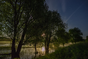 Fototapeta na wymiar Space with stars in the night sky. The landscape with the river and trees is photographed on a long exposure.