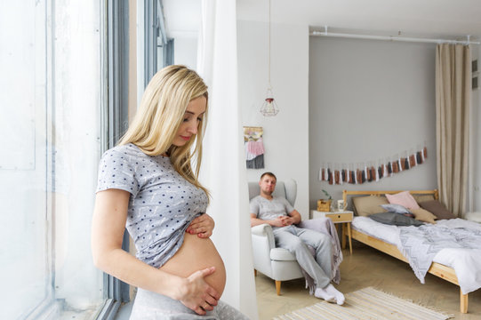 The pregnant woman gently touches the stomach. Her husband is on a background