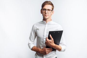 Portrait of a young attractive guy in glasses, in a white shirt, with a folder in his hands, isolated on a white background, for advertising, text insertion