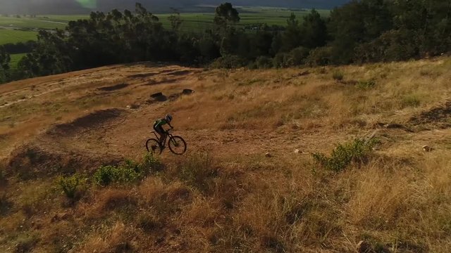 Aerial drone footage of a mountain biker going up hill on a dirt path in South Africa