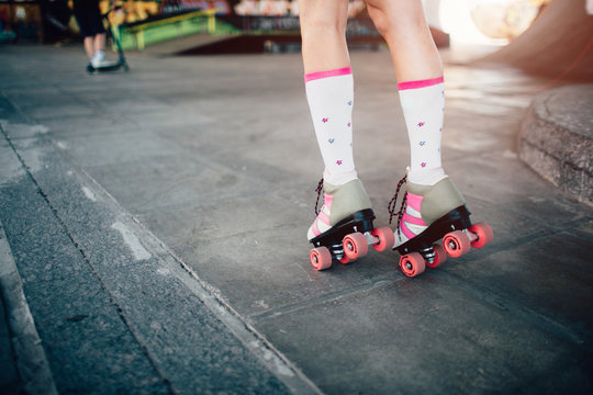 A picture of girl's legs in rollers. She is skating on the road. Also she is posing and standing on toes.