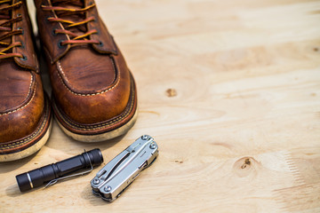 Everyday carry things, Brown leather boots, Black flashlight and Multitool on the wooden board with copy space