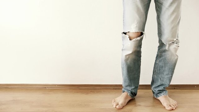 A man in torn-up jeans stands by the wall and stomps with his foot