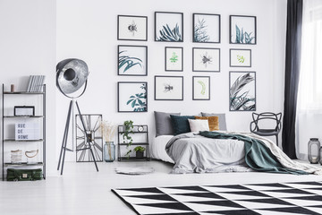 Black and white carpet placed on the floor in bright bedroom interior with king-size bed, black studio lamp and posters hanging on the wall