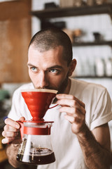 Portrait of young barista standing at bar counter and smelling pour over coffee while thoughtfully looking aside in cafe