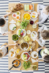 Top view of children eating healthy homemade meal. Wooden table with dishes full of colorful cooked food, eco vegetables, fruit, wholegrain bread rolls and pretzels.