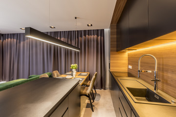 Dark drapes hanging in modern kitchen interior with black shelves and countertop, wooden table and chairs