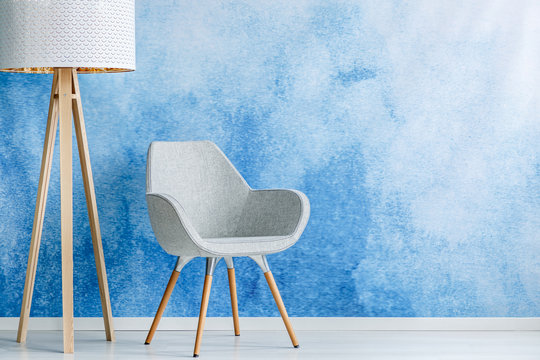 Living room interior with gray armchair and standing lamp against blue and white ombre wall with empty space. Real photo.